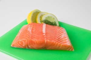 Salmon fillet on plastic cutting board with garnishes